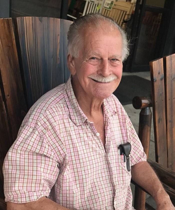 Roma J. Richard Jr. smiling in a wooden rocking chair