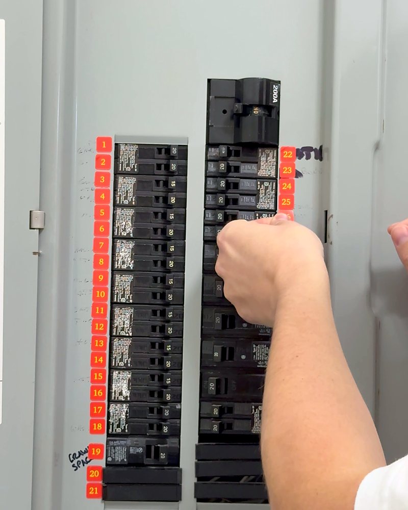 A hand pressing a red Breaker Label with a yellow number next to a breaker in the panel