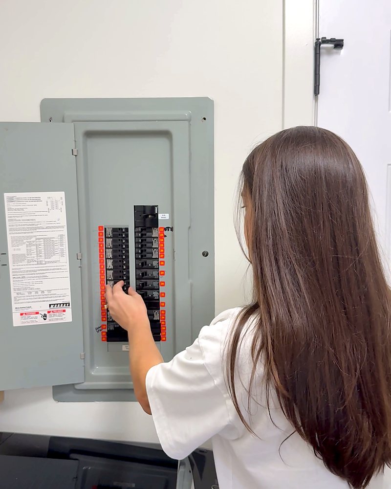 A woman at the open panel switching off one breaker at a time