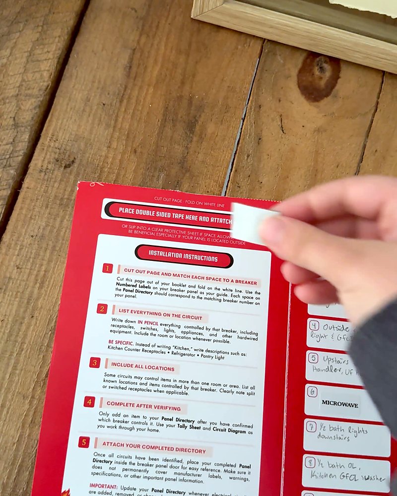 Hands adding tape to the back of the Panel Directory before it goes in the panel door